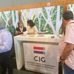 balcão informativo da cig. mulher segura na mão um folheto, enquanto é atendida. pessoas olham para o topo do balcão, onde estão os folhetos informativos