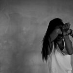 Mulher cobre a cara com os braços e mãos algemadas