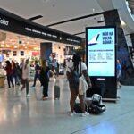 Cartaz afixado num mupi no aeroporto com uma mulher negra a olhar e outras pessoas a passar