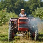 Mulher a conduzir um trator no meio de um pomar com árvores de cada lado