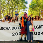 sandra ribeiro e helder bertolo em frente a marchantes do orgulho lgbti+. na faixa, 25.ª marcha do orgulho lgbti+ de lisboa