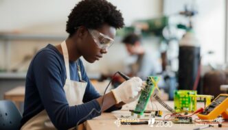 mulher com óculos protetores, solda pequenos componentes eletrónicos numa placa de circuito